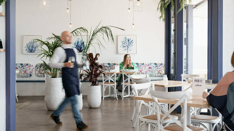 A waiter with a blue apron bringing drinks to a table.