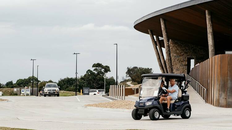 A man driving a golf cart in front of a golf club.