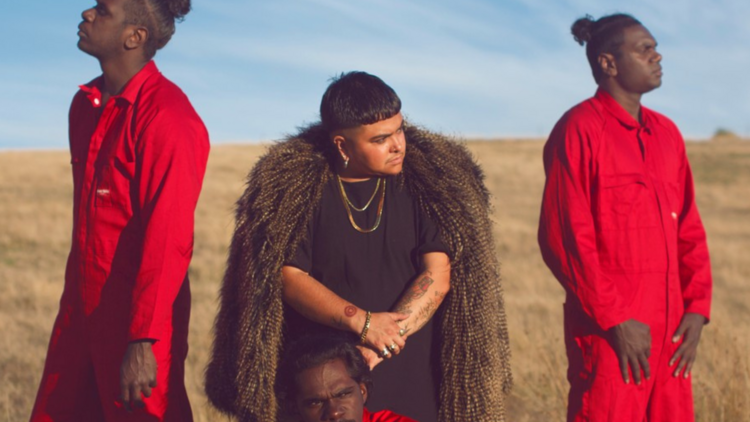 Mo'Ju Artist Mo'Ju poses with people on either side of them in red jumpsuits