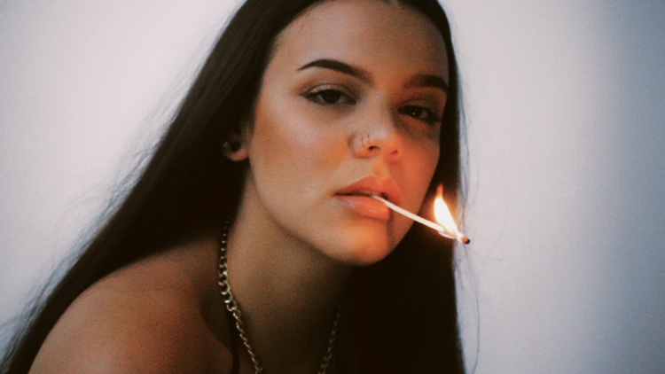 Artist Cloe Terare poses in soft light with a lit match in her mouth
