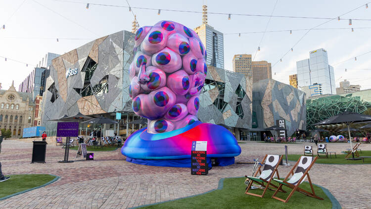 A huge inflatable sculpture of a bust covered in eyes sits in Federation Square