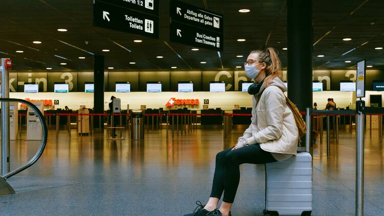 A woman sitting on luggage at the airport.