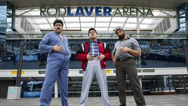 Three men pose in front of Rod Laver Arena with their feet apart and hands on their stomachs.