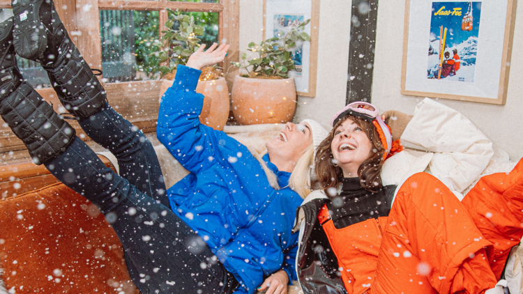 Two girls laugh while lying down and staring up at falling flecks of white snow