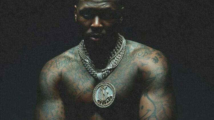 YG stands shirtless against a black background, a gold chain and pendant hang around his neck