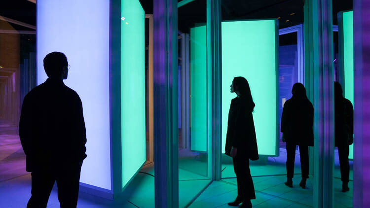 Two people stand in a room with mirrors and coloured light panels.