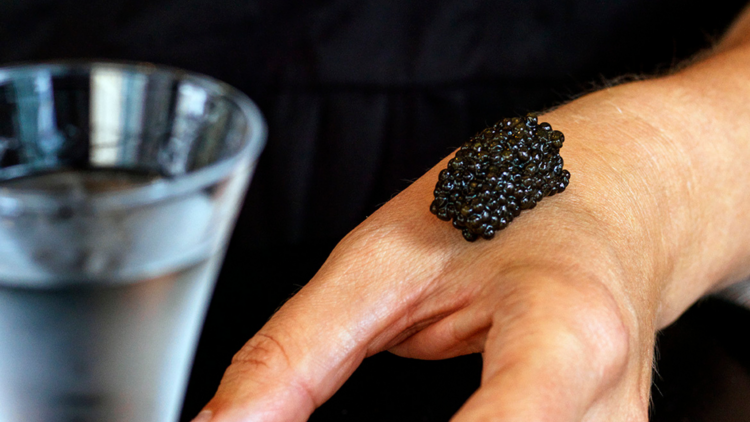 A bump of caviar on a hand next to a glass of vodka