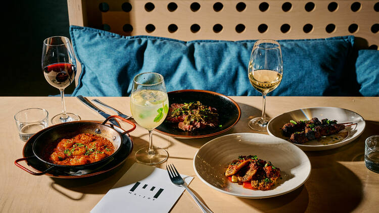 A table with four dishes and three glasses of wine.