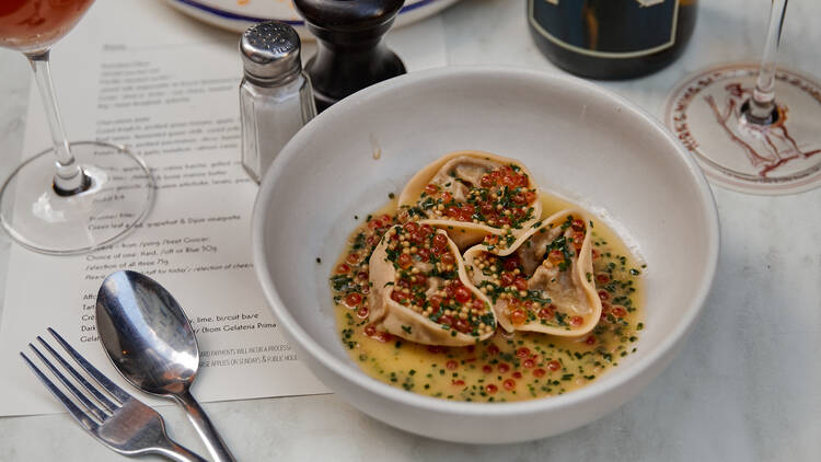 A dish of dumplings covered in sauce, chives and fish roe.