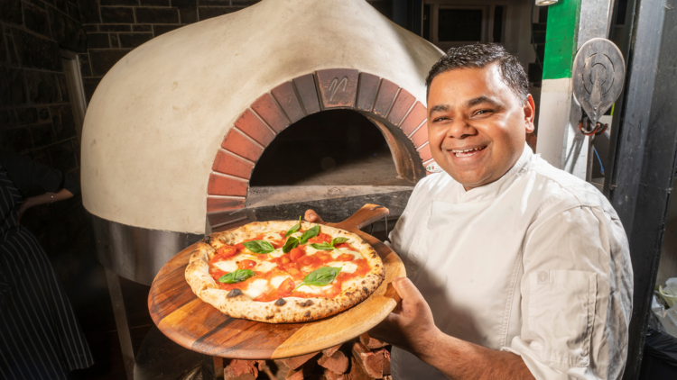 Chef Gagan Bhatnagar holding a pizza in front of a pizza oven.