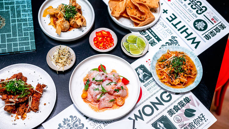 An overhead shot of a table laden with white plates of Asian fusion food – including sashimi, noodles and dumplings.