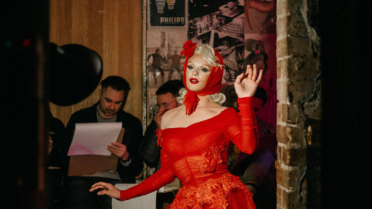 Drag queen Aubrey Haive poses for a live drawing class in a red dress and headscarf