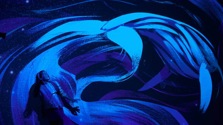 A child stands against a wall lit up with a digital projection of a whale in blue swirling waters