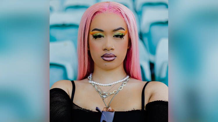 A close-up shot of singer A.Girl with pink hair, layered necklaces and brightly coloured make-up.