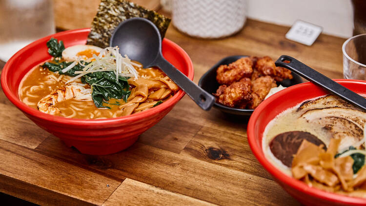 Two bowls of ramen and a bowl of fried chicken sits on top of a wooden table.