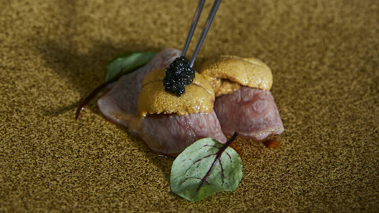 A person picks up caviar on top of wagyu and uni with black chopsticks