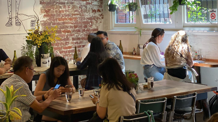 People sit in a cafe, with brick lined walls and a large communal table in the middle