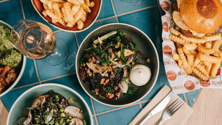 An overhead shot of a blue-tile table with three salad bowls, two burgers with chips and a glass of rosé.