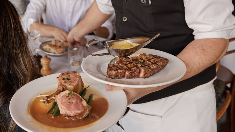 A waiter holding a plate of steaks and lamb cutlets.