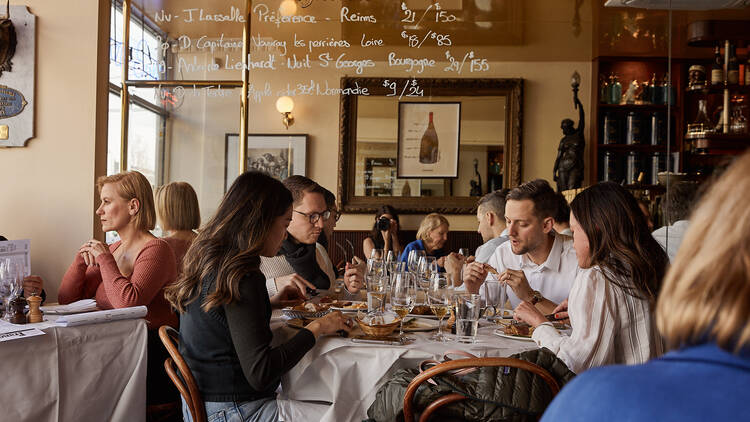 Diners sitting at a table with food and glasses of wine.