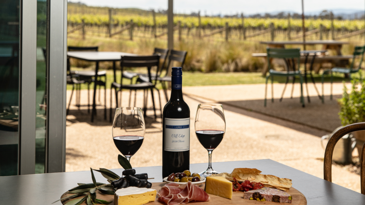 A platter of cheeses and cured meats with a bottle and two glasses of wine.