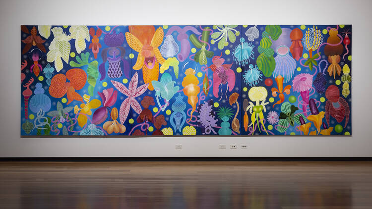 A vibrant, multicoloured painting of graphic flowers sits on a white wall in a gallery