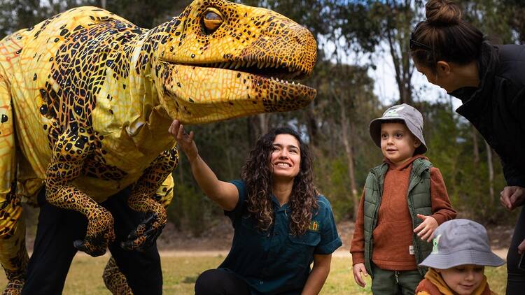 A lifesize dinosaur puppet with a handler and some children
