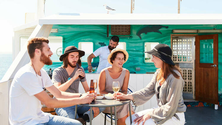 A group of four people sitting on a ferry enjoying drinks and food.