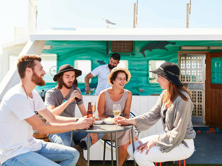 A group of four people sitting on a ferry enjoying drinks and food.