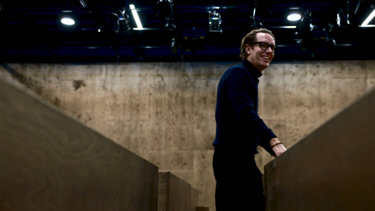 A man in a black skivvy and glasses stands in half-finished theatre.