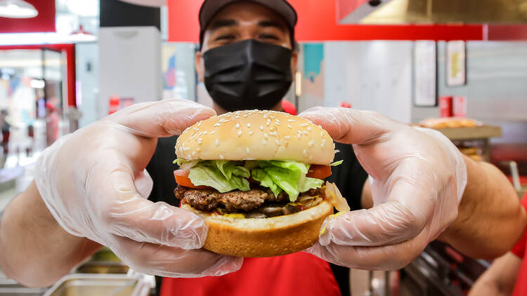 A fast-food worker holding a burger up to the camera.