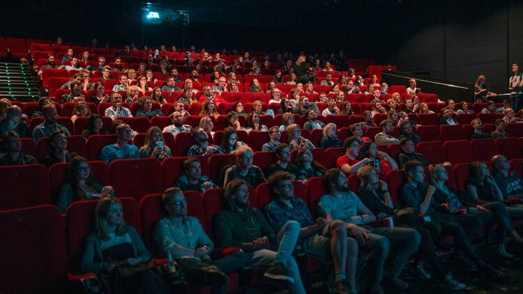 a cinema full of people sitting on red chairs 