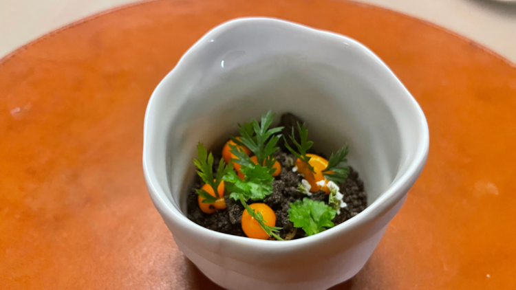 A white tea cup filled with carrots, cheddar and 'soil' made from malt.