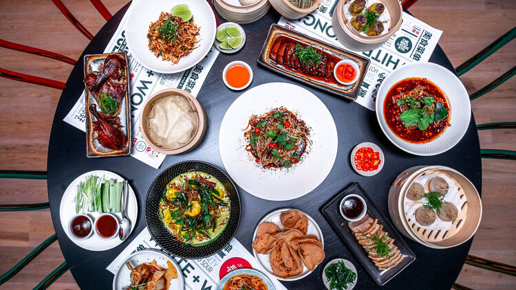 An overhead shot of a round table loaded with Asian dishes like dumplings, stir frys, curries, prawn crackers and peking duck.