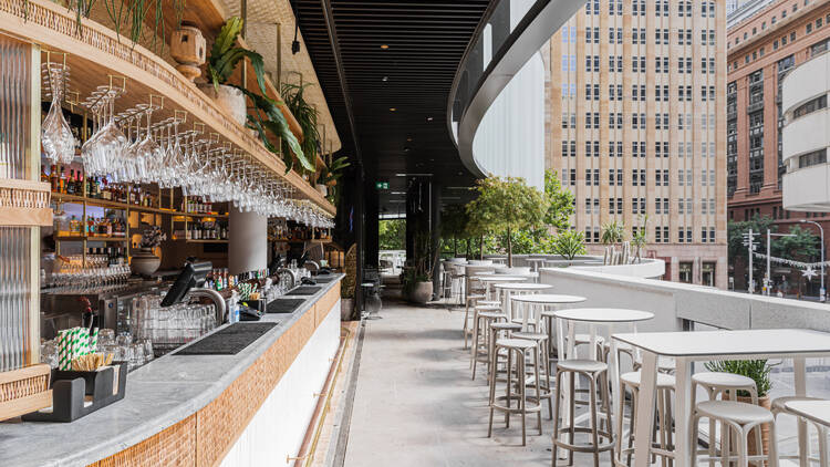 An exterior shot of Cabana Bar with glasses hanging above the bar, outdoor seating and views of Martin Place.