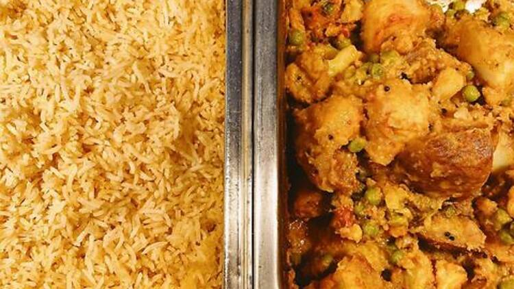 Two chafing dishes full of vegetarian curry and white rice next to each other in a buffet line.