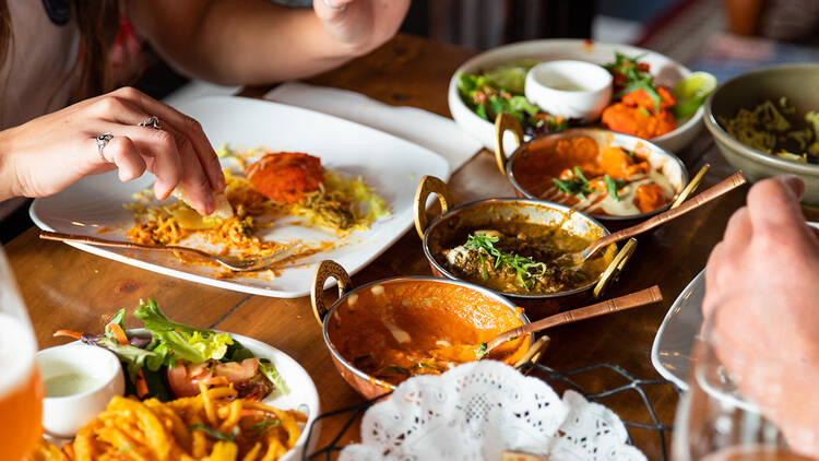 Two people eat from an assortment of plates filled with food at Its Mirchi