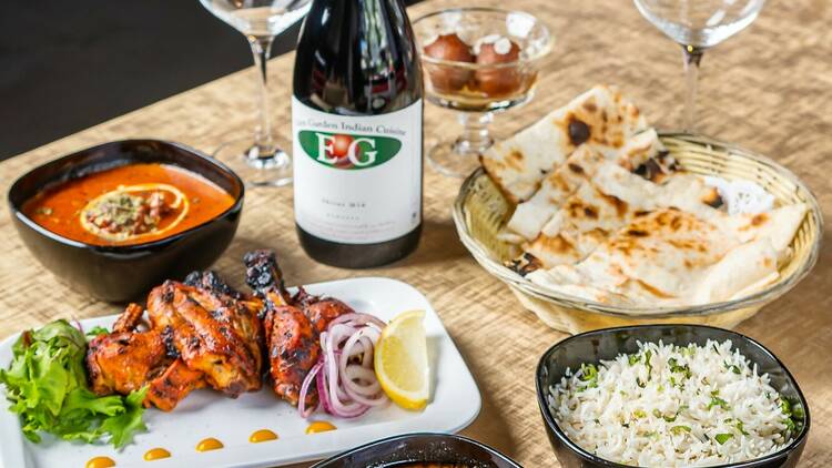 A table with curries, naan, rice, and a bottle of wine with two glasses.