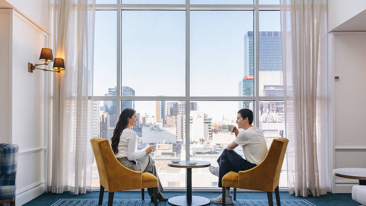 A couple sitting near a window with views of the skyline while drinking coffee.