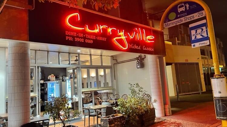 The outside of Curryville, a red neon sign hangs on the wall.