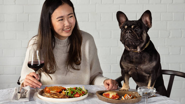 A woman and her dog enjoying dinner together at the table.