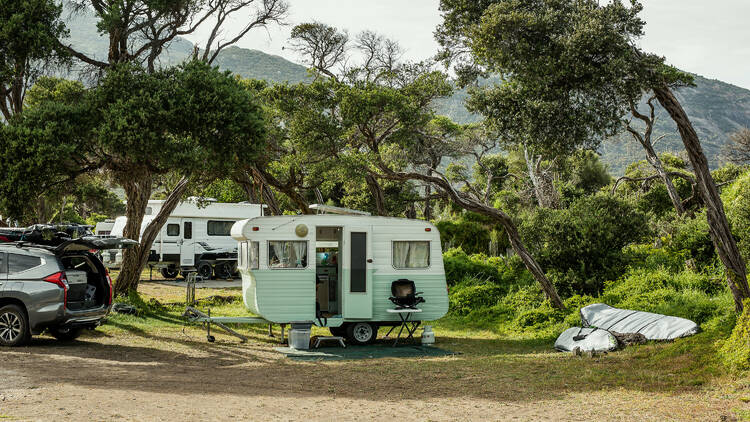 A small white and teal caravan parked in a lot. 