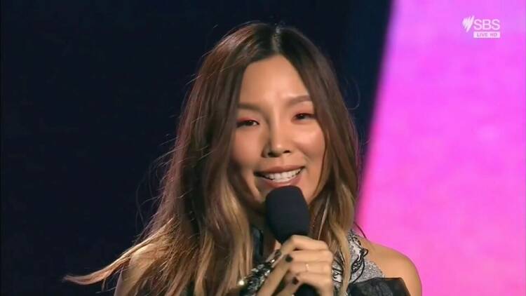 A close-up of singer Dami Im smiling and holding a microphone to her mouth.