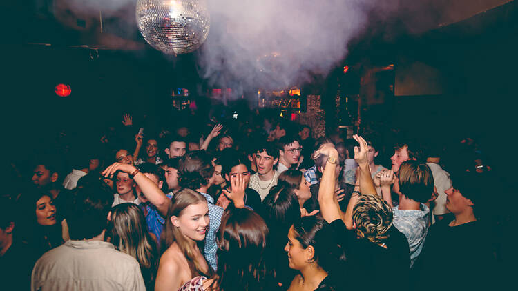 People dance in a club, with a disco ball and smoke