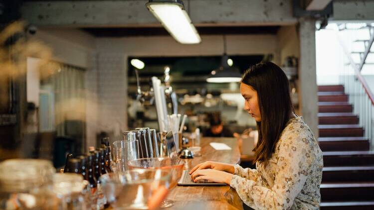 A woman works from her laptop at the bar.