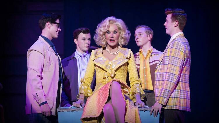 Rhonda Birchmore, in character, sits on a table with four teenage boys surrounding her