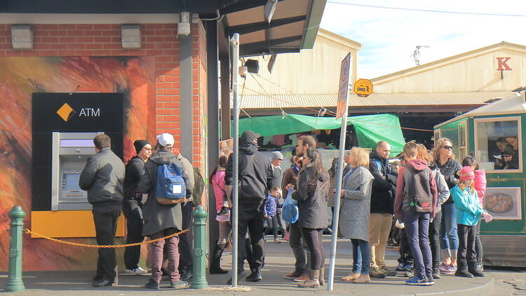 A group of people queuing for an ATM near Queen Vic Market.