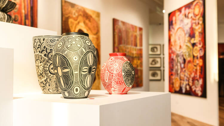 A gallery with white walls features indigenous artworks and pottery