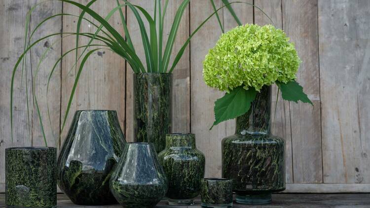 A collection of green glass vases against a wooden backdrop.