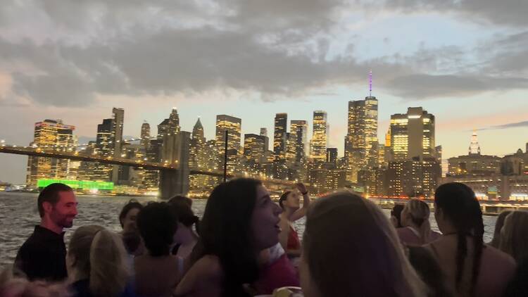 A group of people on a boat deck with the NYC skyline behind them.